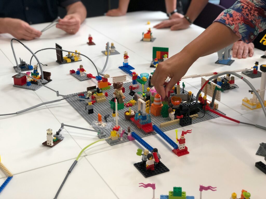 amelie-mourichon-hcLSA1MiU3A-unsplash Menschen die ein gemeinsames Modell mit Lego bauen
