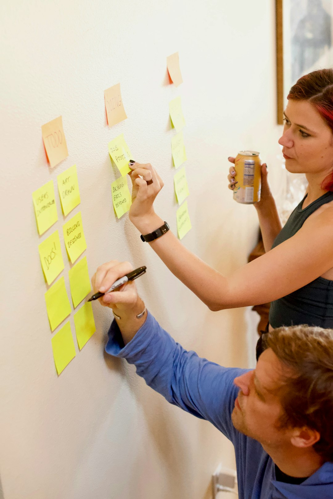 zwei Menschen die Post Its an einer Wand beschriften
