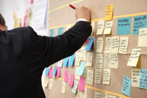 Mensch an einer Metaplanwand mit vielen Post Its der etwas schreibt